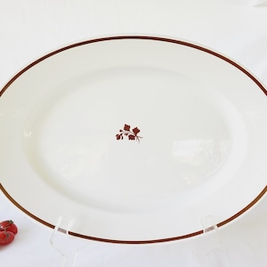 以下が含まれることがあります： 中央に茶色の花柄が描かれた、金色の縁取りのある白い楕円形のサービングプレートです。