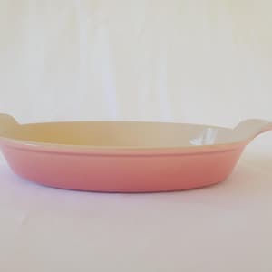 Op de afbeelding: Een roze ovale ovenschaal met twee handvatten. De schaal heeft een lichtroze buitenkant en een crèmekleurige binnenkant. De schaal is gemaakt van keramiek en is geschikt voor het bakken van ovenschotels, desserts en andere gerechten.