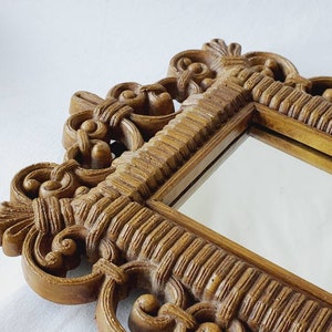 Puede incluir: Primer plano de un espejo decorativo con un marco ornamentado. El marco es de color marr&oacute;n dorado c&aacute;lido y presenta intrincados adornos y detalles texturizados. La superficie del espejo refleja el entorno.