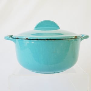 Puede incluir: Una olla de hierro fundido esmaltada de color azul turquesa con tapa. La olla tiene dos asas y un pomo en la tapa.