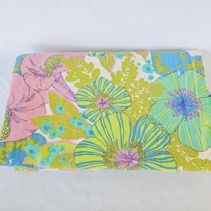 Op de afbeelding: Gevouwen vintage stof met een groot bloemenpatroon. Het ontwerp toont oversized bloemen in tinten roze, limoengroen en turkooisblauw op een witte achtergrond. De stof is netjes opgevouwen en toont de levendige kleuren en het gedurfde ontwerp.