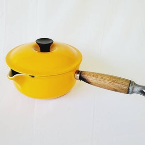 May include: Yellow enamel cast iron saucepan with a wooden handle and a black knob on the lid.