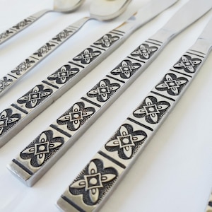 May include: Set of five silver-toned flatware pieces with black floral designs. The pieces include a fork, knife, and three spoons.
