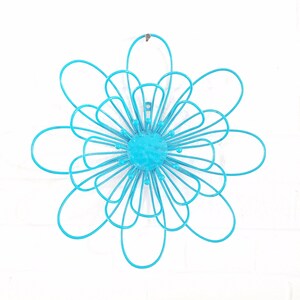 May include: A turquoise blue metal flower wall decor with a circular center and multiple overlapping petals.