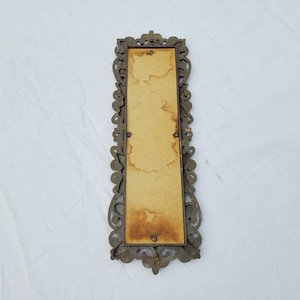 Puede incluir: Un marco de fotos rectangular antiguo con un dise&ntilde;o de filigrana de metal de color bronce ornamentado. El marco tiene un respaldo marr&oacute;n claro con manchas visibles. El marco est&aacute; vac&iacute;o y listo para una foto o una obra de arte.