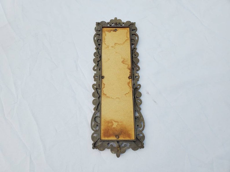 Puede incluir: Un marco de fotos rectangular antiguo con un dise&ntilde;o de filigrana de metal de color bronce ornamentado. El marco tiene un respaldo marr&oacute;n claro con manchas visibles. El marco est&aacute; vac&iacute;o y listo para una foto o una obra de arte.