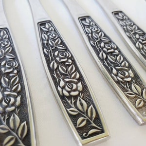 May include: Set of six silver-toned flatware pieces with a rose design. The handles are decorated with an embossed floral pattern.