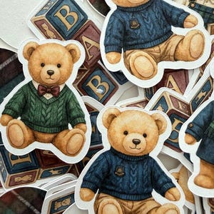 May include: A collection of sticker cutouts featuring teddy bears in various outfits. The bears are depicted in a seated position, wearing sweaters and bow ties. Some stickers include alphabet blocks in the background. The color palette includes shades of brown, blue, and green.