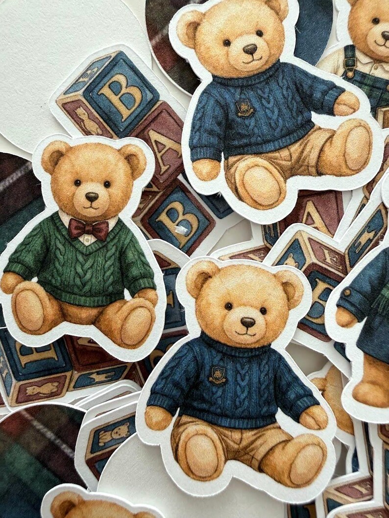 May include: A collection of sticker cutouts featuring teddy bears in various outfits. The bears are depicted in a seated position, wearing sweaters and bow ties. Some stickers include alphabet blocks in the background. The color palette includes shades of brown, blue, and green.