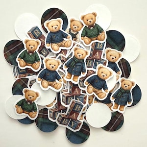 May include: A collection of teddy bear stickers in various outfits, including sweaters and coats, with matching plaid and white circle accents. Some bears are sitting on alphabet blocks. The color palette includes shades of brown, blue, green, and white.