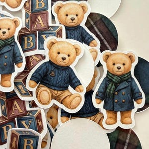 May include: A collection of paper cutouts featuring teddy bears in various outfits. Some bears wear blue sweaters, others wear coats and scarves. Wooden alphabet blocks and white circles are also present.