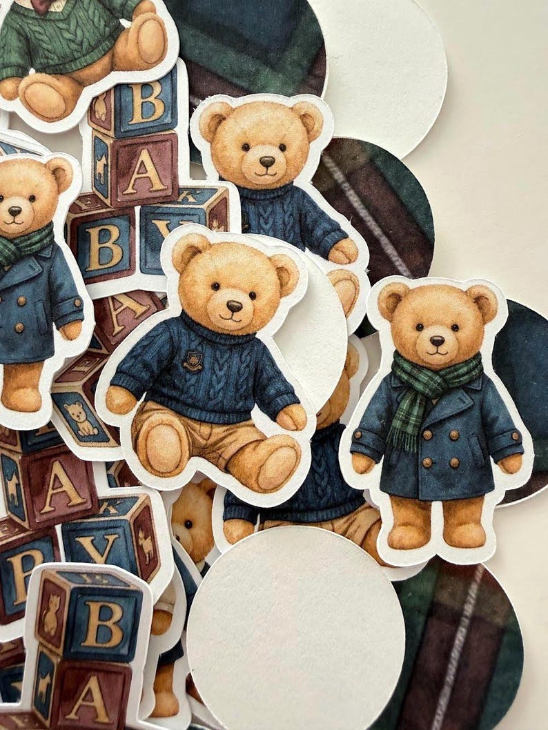 May include: A collection of paper cutouts featuring teddy bears in various outfits. Some bears wear blue sweaters, others wear coats and scarves. Wooden alphabet blocks and white circles are also present.