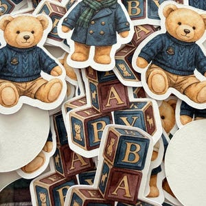 May include: A collection of stickers featuring watercolor illustrations of teddy bears in various outfits, including a blue sweater and a navy coat with a green scarf. Also included are alphabet blocks with the letters A, B, and Y.