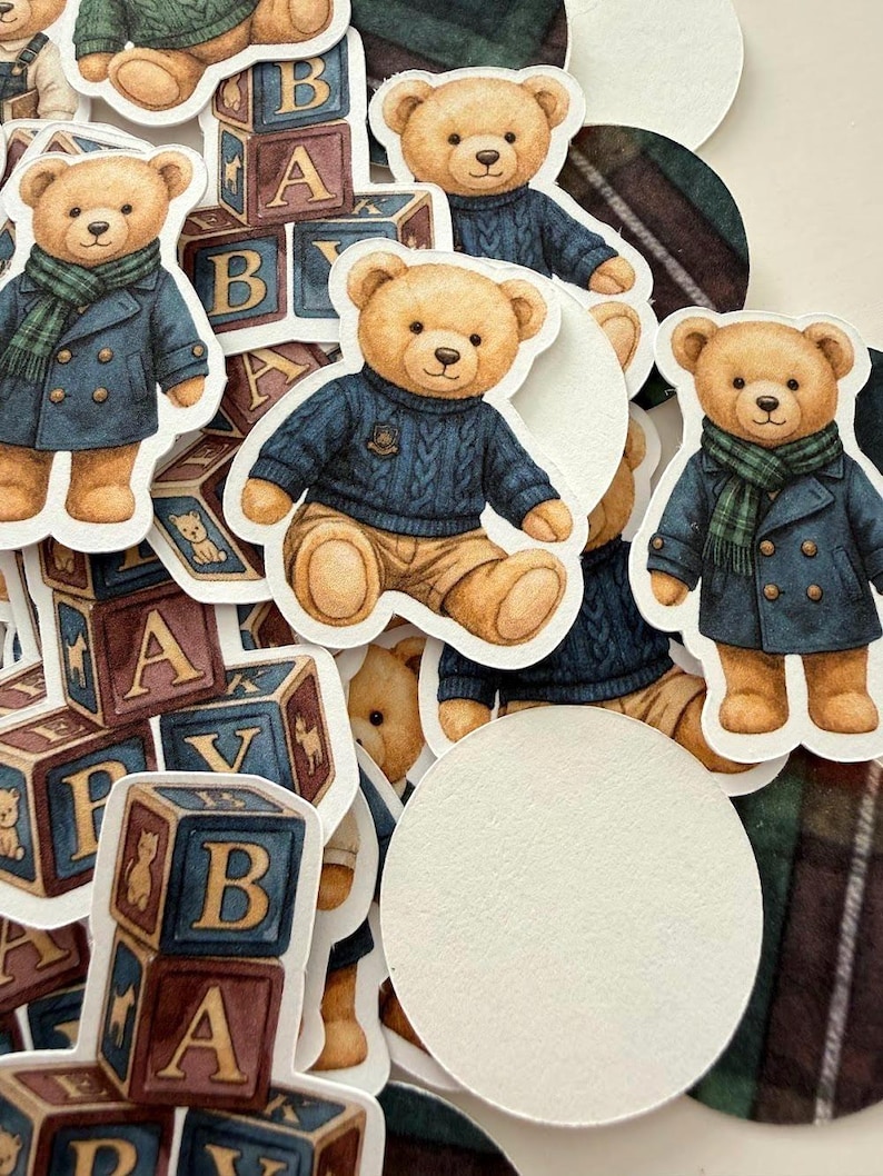 May include: A collection of die-cut stickers featuring teddy bears in various outfits. Some bears wear blue sweaters, others wear blue coats with green scarves. Wooden alphabet blocks are also present.