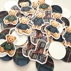 May include: A collection of paper cutouts featuring teddy bears in various outfits, including sweaters and coats. The bears are surrounded by baby blocks and plaid and white circles. The blocks spell out "BABY".
