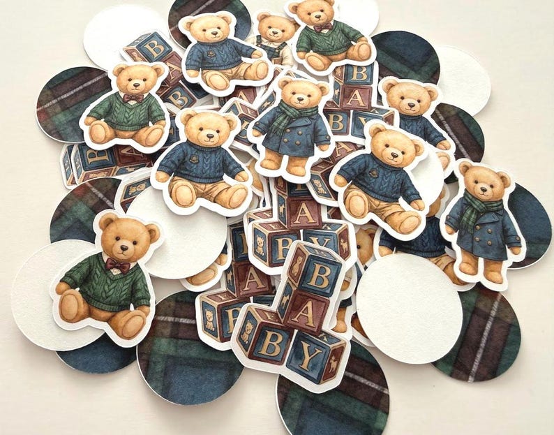 May include: A collection of paper cutouts featuring teddy bears in various outfits, including sweaters and coats. The bears are surrounded by baby blocks and plaid and white circles. The blocks spell out "BABY".