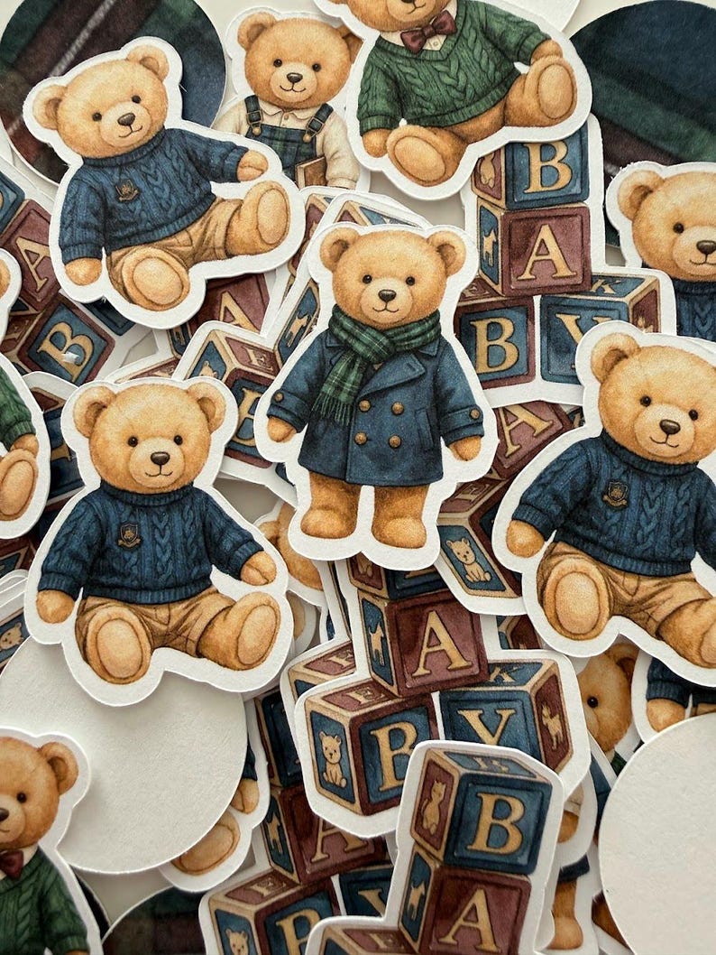 May include: A collection of die-cut stickers featuring teddy bears in various outfits. The bears are dressed in sweaters, coats, and scarves, with some sitting near alphabet blocks. The color palette includes shades of brown, blue, and green.