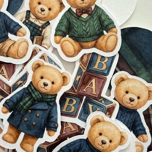 May include: A collection of die-cut stickers featuring teddy bears in various outfits. The bears are depicted in a range of attire, including sweaters, coats, and overalls. Some stickers include alphabet blocks. The color palette includes shades of brown, blue, and green.