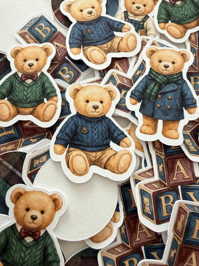 May include: A collection of die-cut stickers featuring teddy bears in various outfits. The bears are wearing sweaters, coats, and bow ties. Wooden alphabet blocks with the letters A and B are scattered around the stickers.