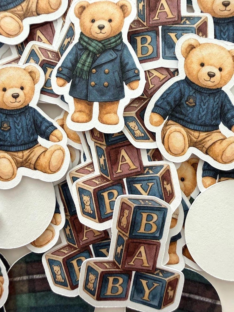 May include: A collection of stickers featuring watercolor illustrations of teddy bears in various outfits, including a blue coat and a cable-knit sweater. Also included are alphabet blocks with the letters A, B, and Y, and the word "BABY".
