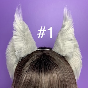 May include: A pair of gray furry animal ears on a headband. The headband is worn on a person with brown hair. The text #1 is visible in the image.