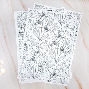 Op de afbeelding: Een set van drie vellen wit papier met een zwart-witte lijntekening van lelies en bladeren. De vellen zijn op elkaar gestapeld.