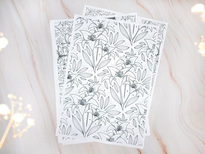 Op de afbeelding: Een set van drie vellen wit papier met een zwart-witte lijntekening van lelies en bladeren. De vellen zijn op elkaar gestapeld.