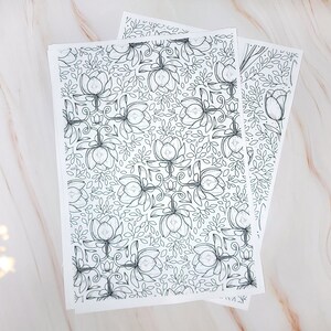 Op de afbeelding: Twee vellen wit papier met een zwart-wit bloemenpatroon. Het patroon is een herhalend ontwerp van gestileerde bloemen en bladeren.