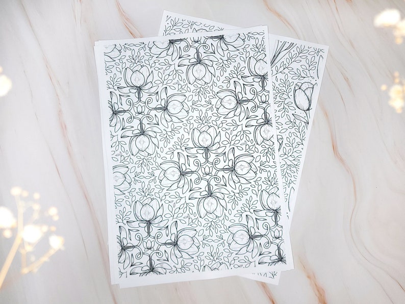 Op de afbeelding: Twee vellen wit papier met een zwart-wit bloemenpatroon. Het patroon is een herhalend ontwerp van gestileerde bloemen en bladeren.