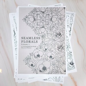 Op de afbeelding: Een zwart-wit kleurboek met de titel "Seamless Florals, Volume 1: A Coloring Book for People Who Love Flowers". De omslag heeft een bloemmotief met een herhalend patroon van bloemen en bladeren.
