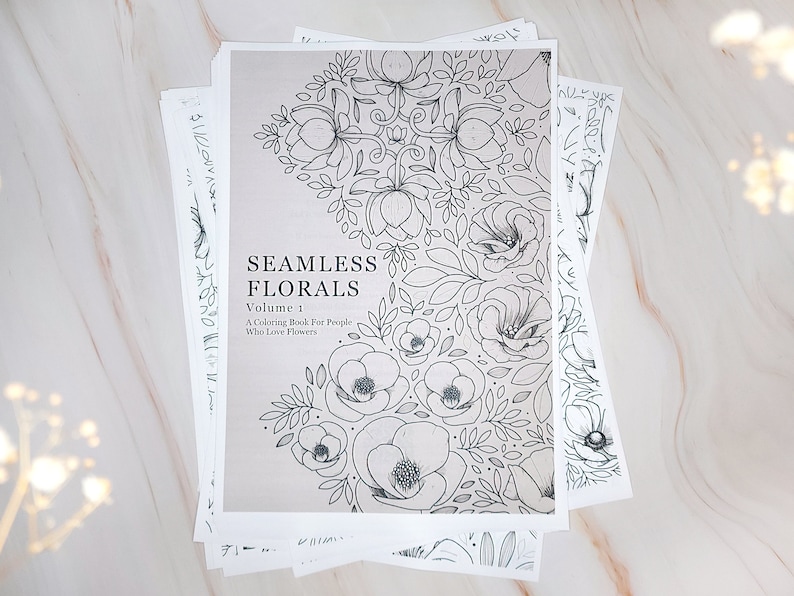 Op de afbeelding: Een zwart-wit kleurboek met de titel "Seamless Florals, Volume 1: A Coloring Book for People Who Love Flowers". De omslag heeft een bloemmotief met een herhalend patroon van bloemen en bladeren.
