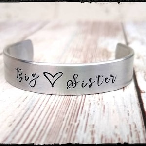 May include: Silver bracelet with the words "Big Sister" and a heart symbol engraved on it.
