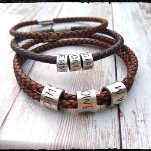 May include: A brown leather bracelet with silver beads engraved with the names "Nick", "Greg", "Emma", "Owen", "Will", and "Olivia".