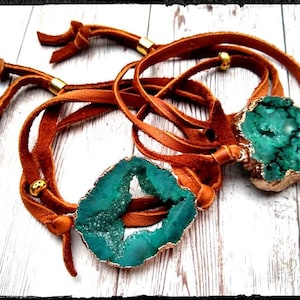 May include: Two leather bracelets with green agate stone charms. The bracelets are brown leather with gold accents.