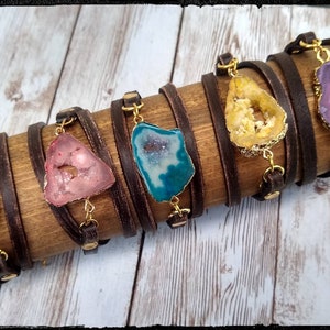 May include: Six leather wrap bracelets with different colored agate slices. Each bracelet has a gold chain and a gold clasp.