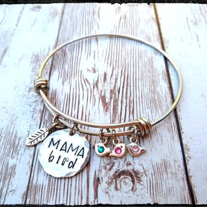 May include: A silver bangle bracelet with a charm that says "MAMA bird" and a small leaf charm. There are also three small bird charms with rhinestones.