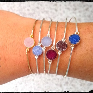 May include: Five silver bangle bracelets with different colored agate stone charms. The charms are in shades of pink, blue, gray, purple, and blue.