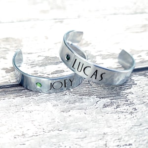 May include: Two silver bracelets with green gemstones. The bracelets are engraved with the names "LUCAS" and "JOEY".