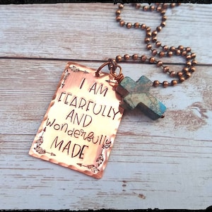May include: A copper necklace with a pendant that reads "I am fearfully and wonderfully made". The pendant is attached to a copper chain with a turquoise cross charm.