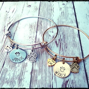 May include: Two expandable charm bracelets, one silver and one gold, with charms that say "My Dog" and "My Cat" with paw prints and the name "Jinx" on each.