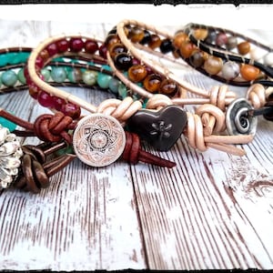 Puede incluir: Cuatro pulseras de cuero con cuentas de piedras preciosas y detalles metálicos. Las pulseras presentan un dije de girasol, un dije de corazón, un dije de mandala y un dije redondo con un diseño de espiral.