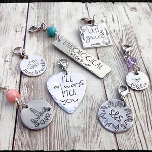 Pode incluir: Uma coleção de sete pingentes de prata com vários designs e textos. Os pingentes incluem um pingente em forma de coração com o texto "I'll always pick you", um pingente redondo com um design de unicórnio e o texto "Ava", um pingente redondo com um design de flor e o texto "Just breathe", um pingente quadrado com o texto "Grit & grace", um pingente retangular com o texto "Unbiological Sister", um pingente redondo com um design de pássaro e o texto "Chloe", e um pingente redondo com o texto "S&S" rodeado de flechas.