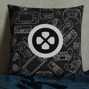 May include: Black and white throw pillow with a pattern of video game controllers and consoles. The pillow features a white circle with a black gamepad icon in the centre.