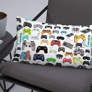 May include: White pillow with a colorful pattern of video game controllers. The controllers are in various colors and styles, including classic and modern designs.