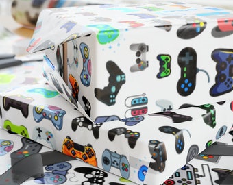 May include: White wrapping paper featuring a repeating pattern of colorful video game controllers in various styles, including black, blue, green, and orange designs. The paper is shown wrapped around a rectangular box with scissors nearby.