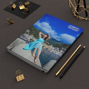 May include: A blue hardcover photo album with a photo of a woman in a blue dress sitting on a rock by the ocean. The album has the name "Elizabeth" printed on the cover.