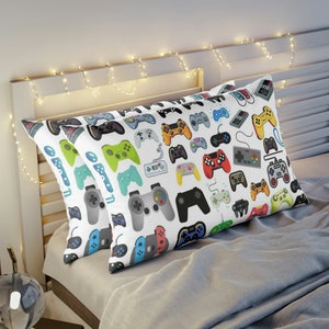 May include: Two white pillowcases with a pattern of colorful video game controllers. The pillowcases are on a gray bed with a white headboard and string lights.