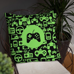 May include: Black cushion with a neon green gaming controller design. The cushion features a repeating pattern of gaming consoles, controllers, and steering wheels. A large green circle in the centre highlights a controller graphic.