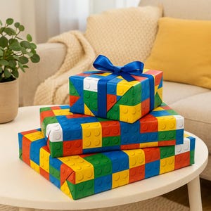 May include: Three gift boxes wrapped in colourful patterned paper with a blue ribbon on the top box. The paper features a repeating pattern of red, yellow, green, and blue squares that resemble Lego bricks.