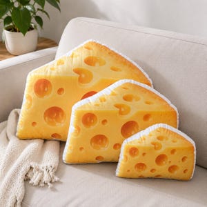 May include: Three wedge-shaped throw pillows designed to look like blocks of Swiss cheese. Each pillow features a vibrant yellow color with a realistic print of various sized circular holes throughout the surface and white piped edges.